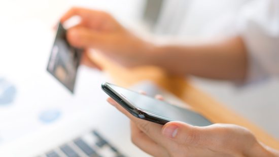 Hands holding a credit card using laptop computer and mobile phone for online shopping .